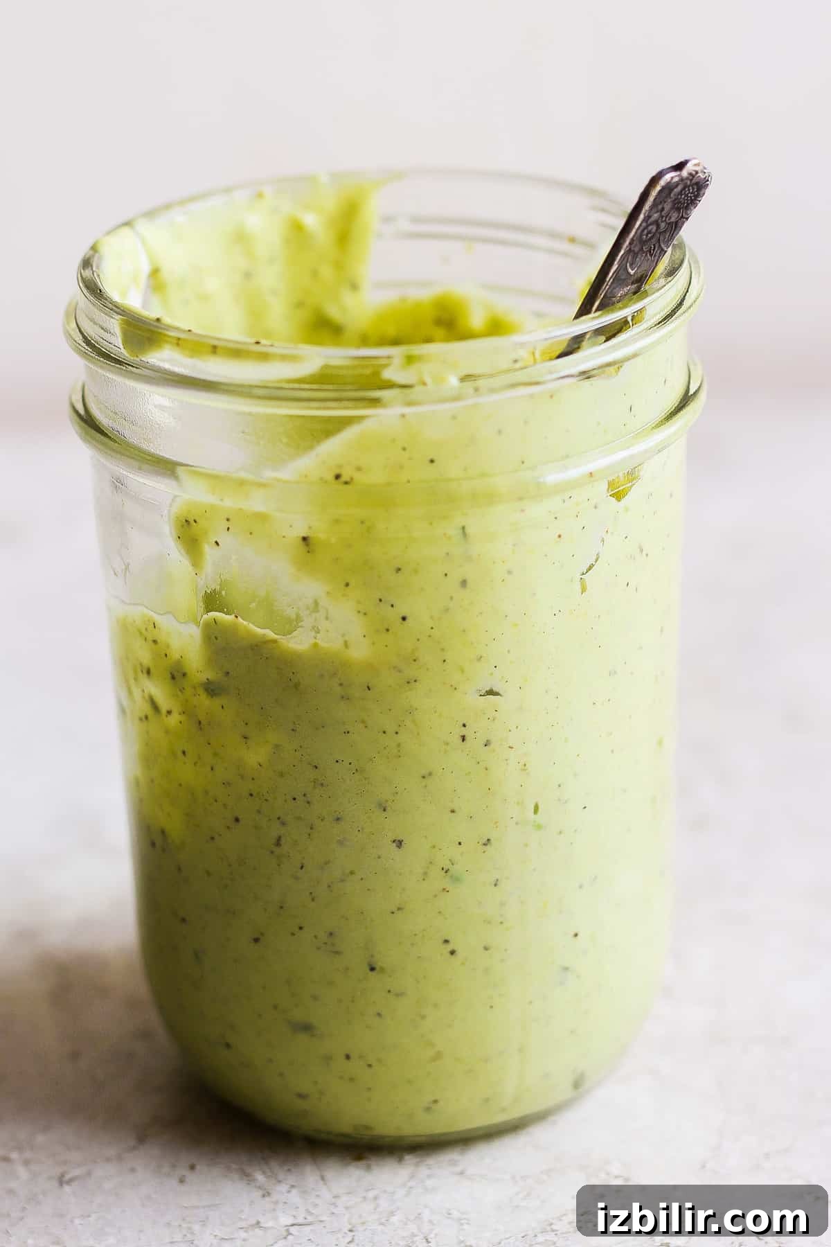 A jar of green sauce with a spoon in it.