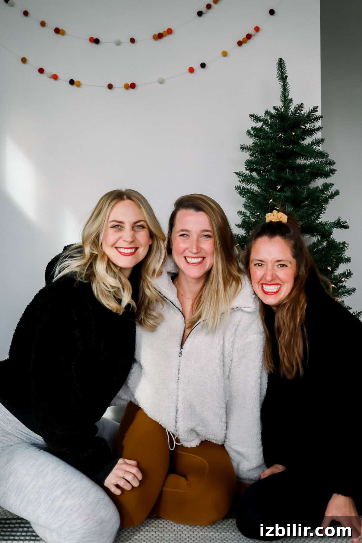 Three women sitting in front of a Christmas tree wearing lululemon holiday styles