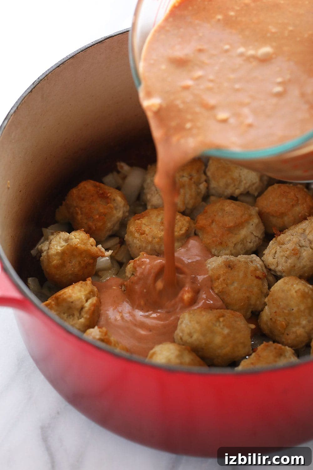 Pouring tikka masala sauce over the meatballs