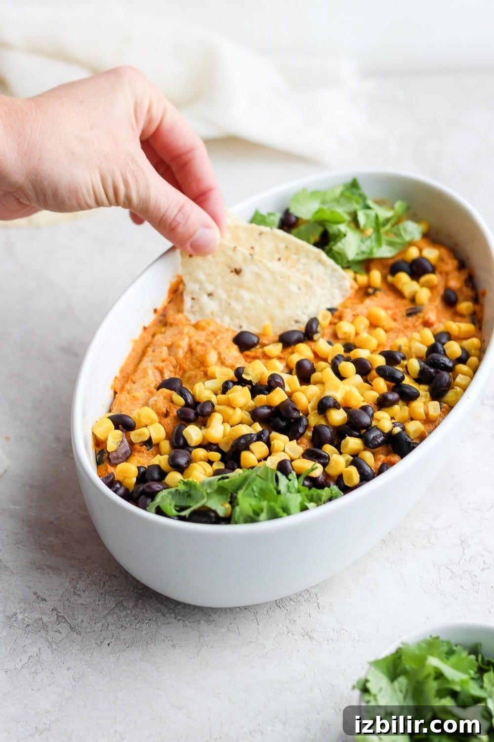 Dipping tortilla chip into Vegan Street Corn Queso vegan street corn queso dip with a tortilla chip being dipped in it