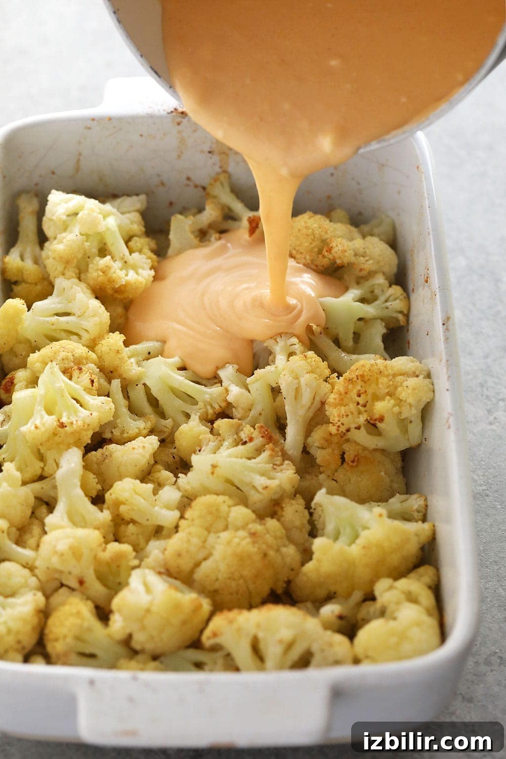 Pouring cheese sauce over roasted cauliflower cauliflower mac and cheese with the sauce being poured over cauliflower