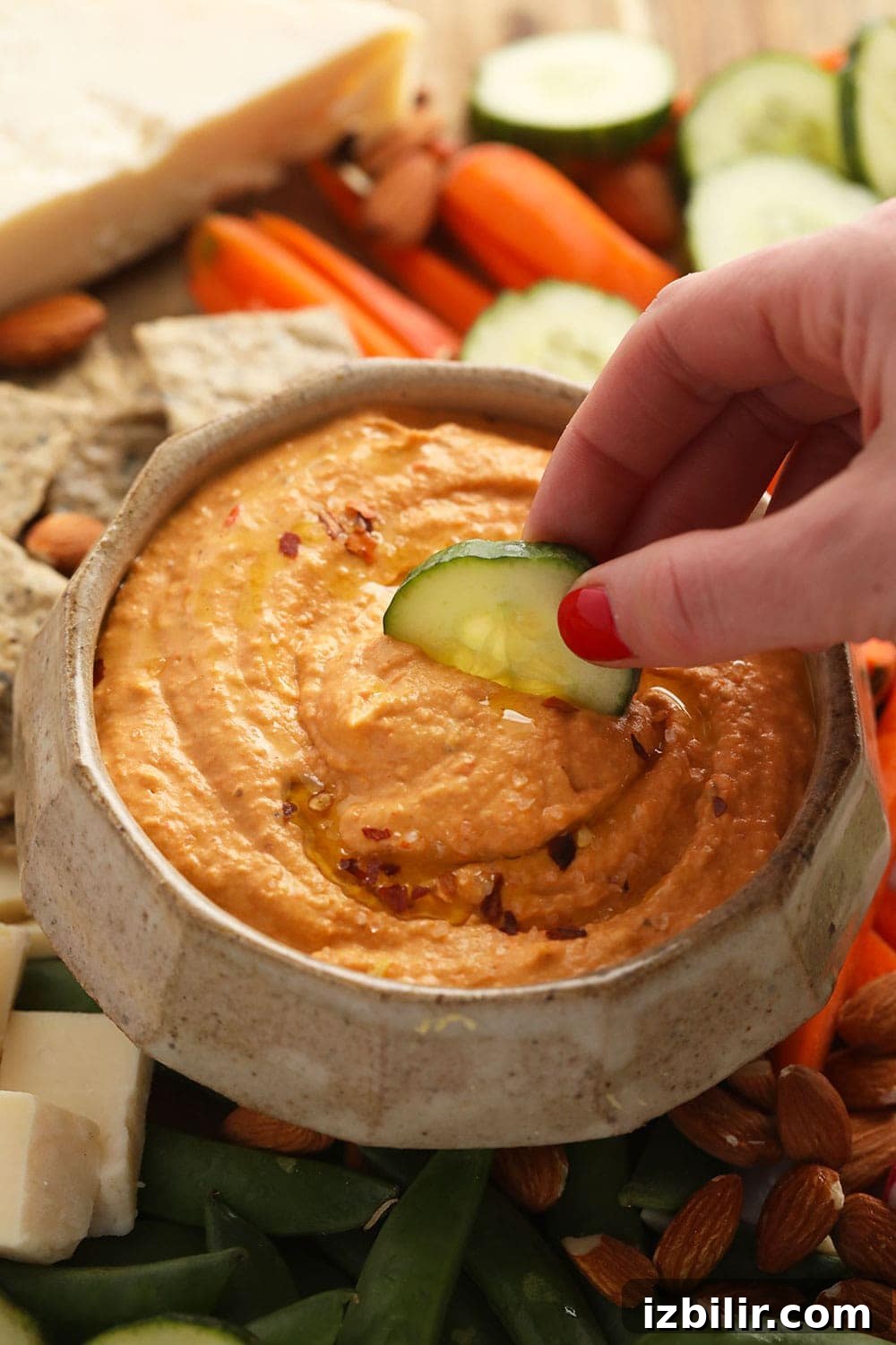 Roasted Red Pepper Hummus roasted red pepper hummus with a cucumber being dipped in it