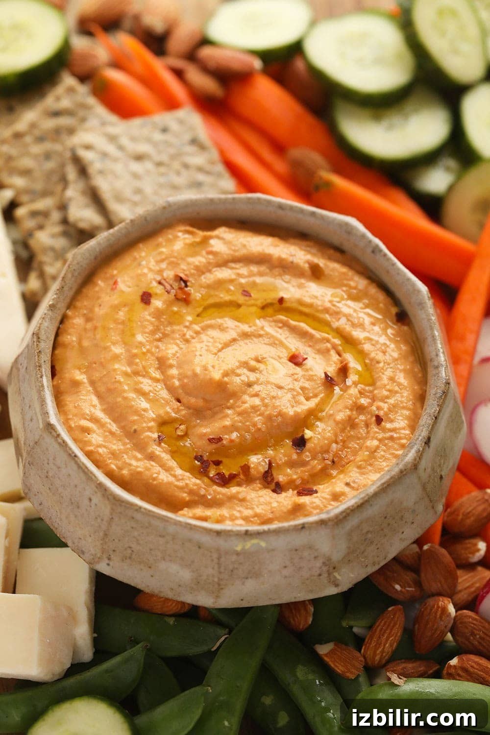 Hummus served with crackers and vegetables roasted red pepper hummus surrounded by crackers, sliced veggies and crackers