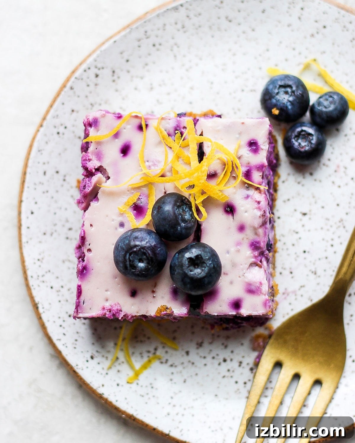 blueberry cheesecake bar on a plate topped with fresh blueberries and lemon zest.