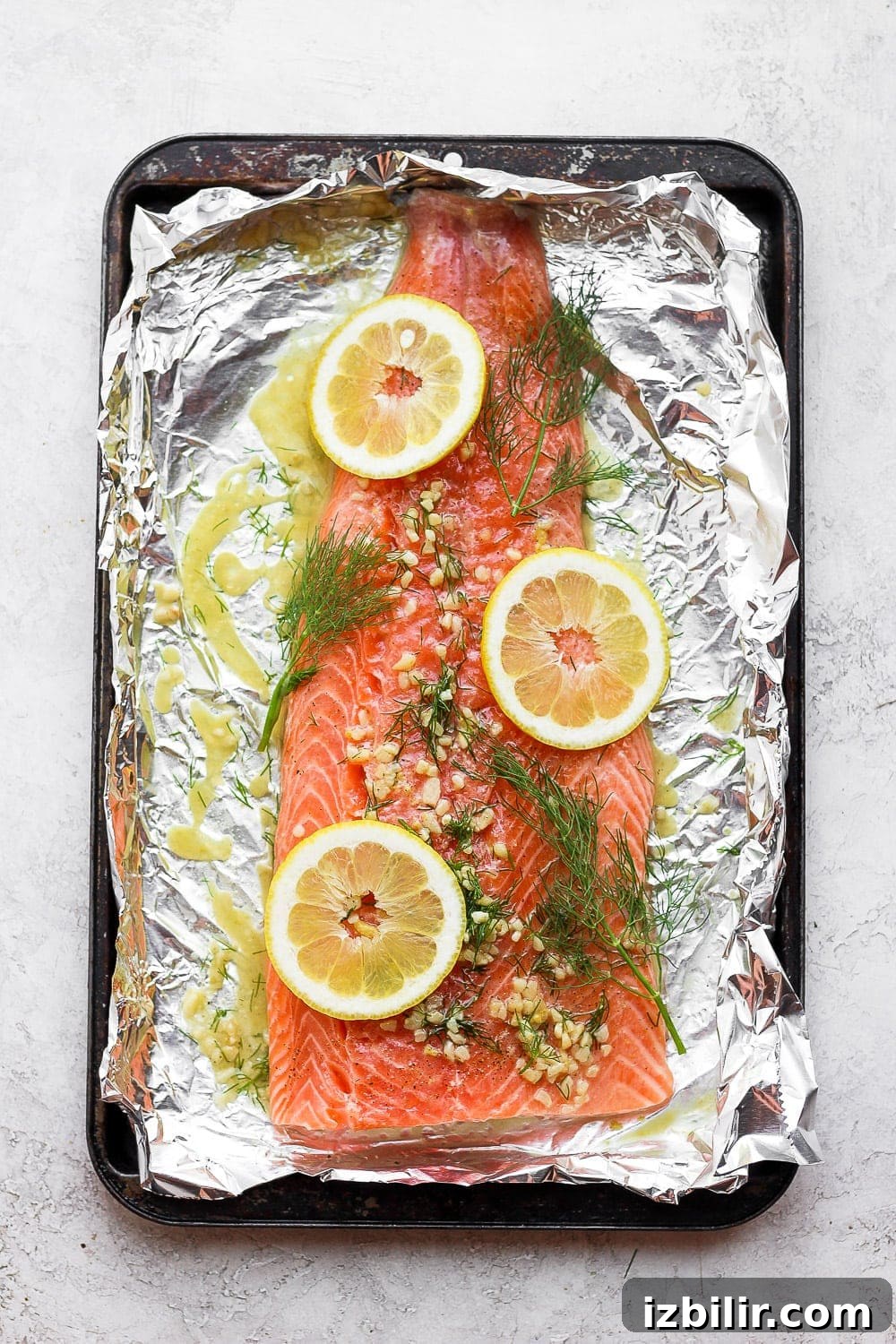 large salmon fillet on tin foil with lemons, dill, and garlic
