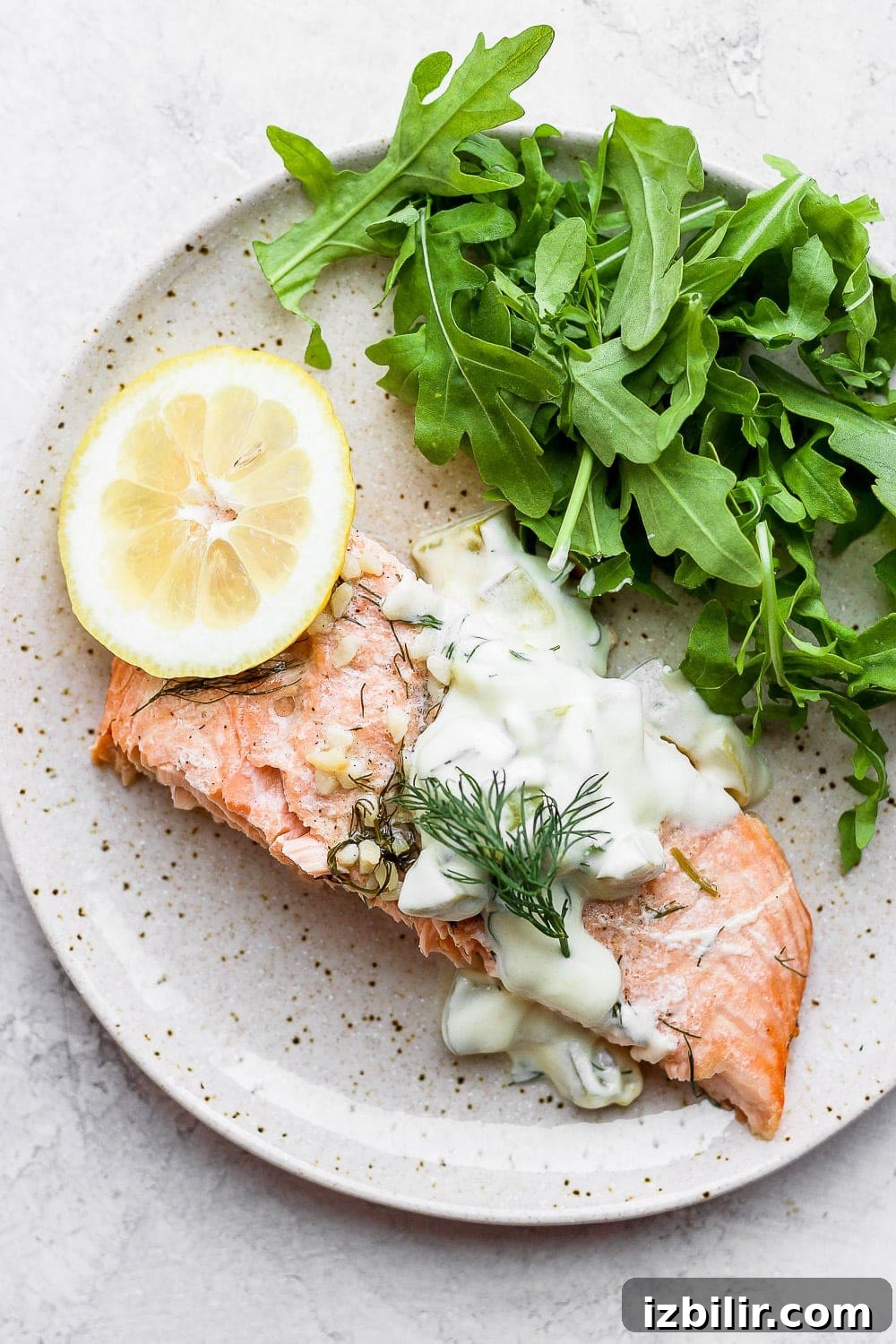salmon portion on plate with arugula, lemon, and tartar sauce