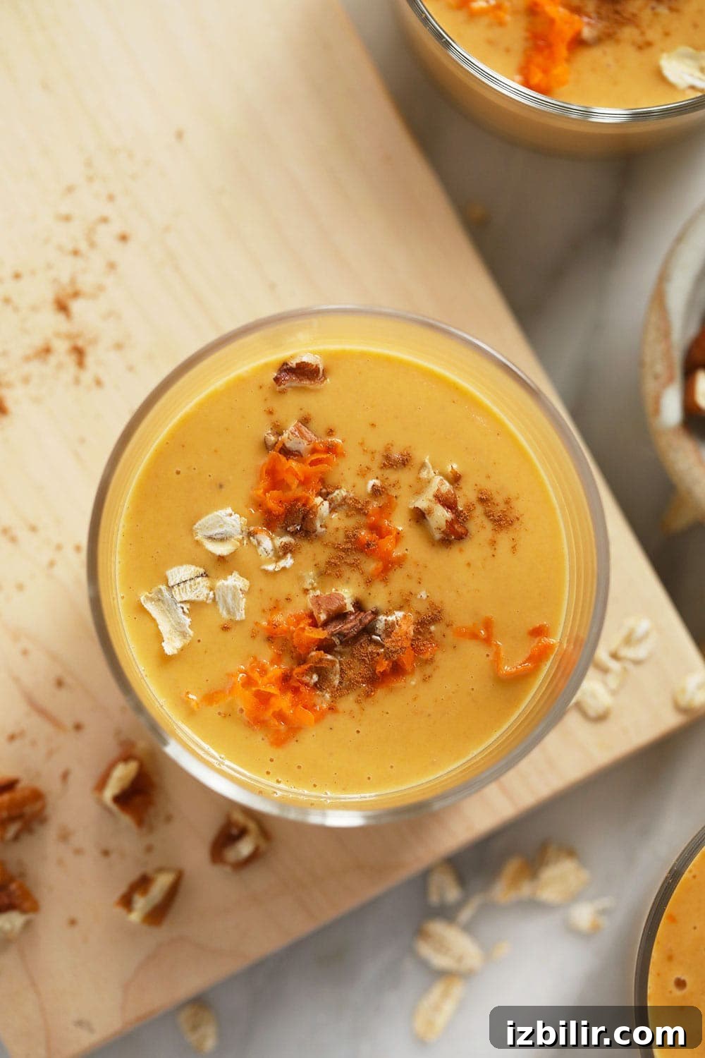A glass with carrot cake smoothie topped with walnuts, oats, and shredded carrot.
