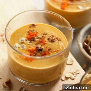 A bowl of carrot cake smoothie with oats on a wooden cutting board.