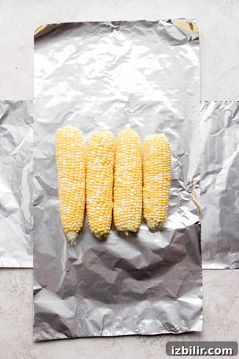 Foil-Wrapped Corn on the Grill 3 tin foil laid out with 4 ears of corn on it