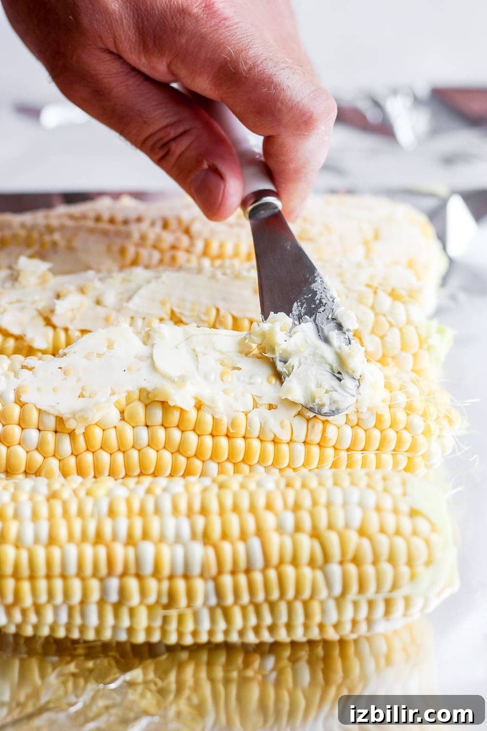 Foil-Wrapped Corn on the Grill 4 softened butter being spread on ears of corn before it goes on the grill