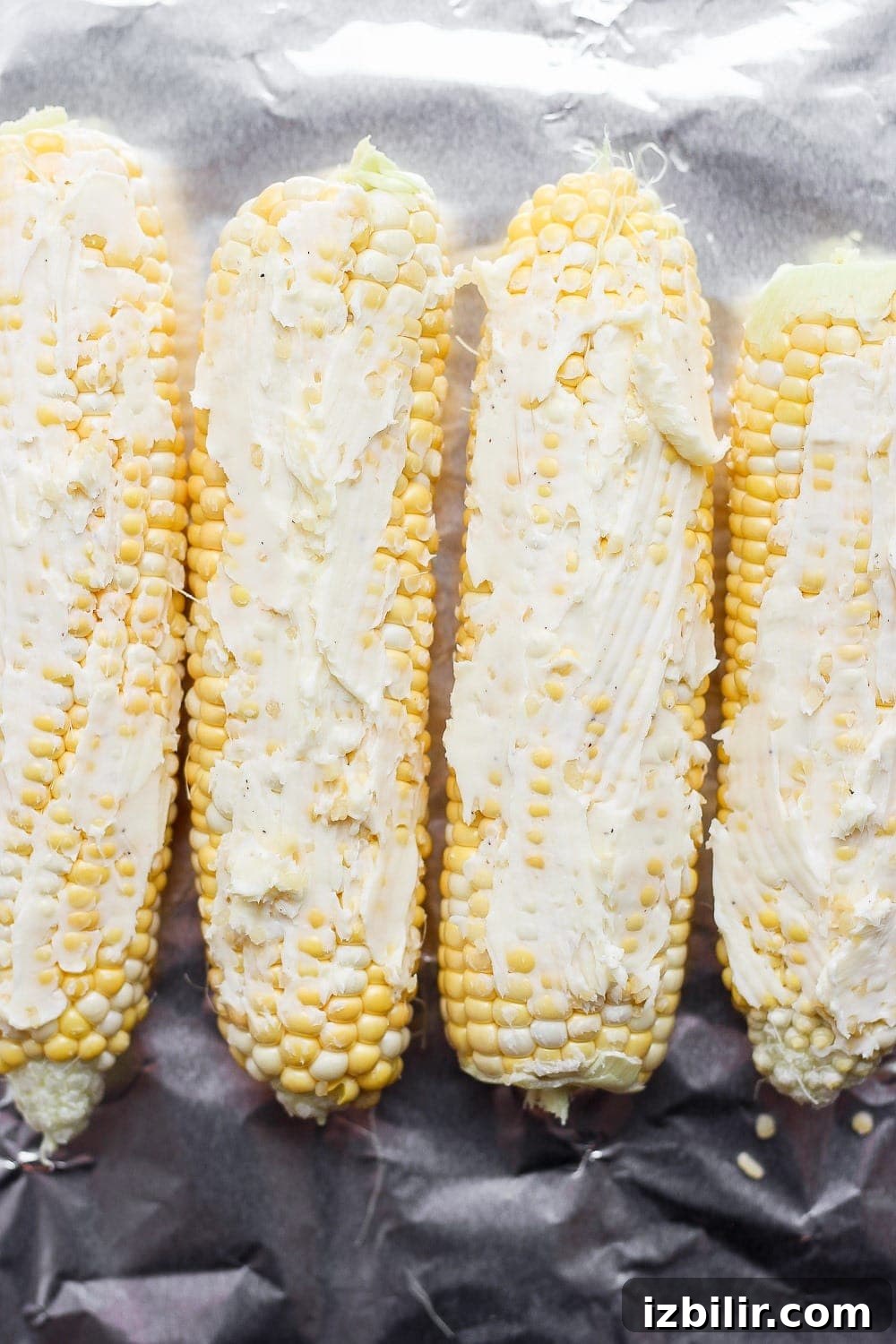 Foil-Wrapped Corn on the Grill 5 corn on the cob with butter spread on it, laid atop tin foil and ready to be made into a foil pack