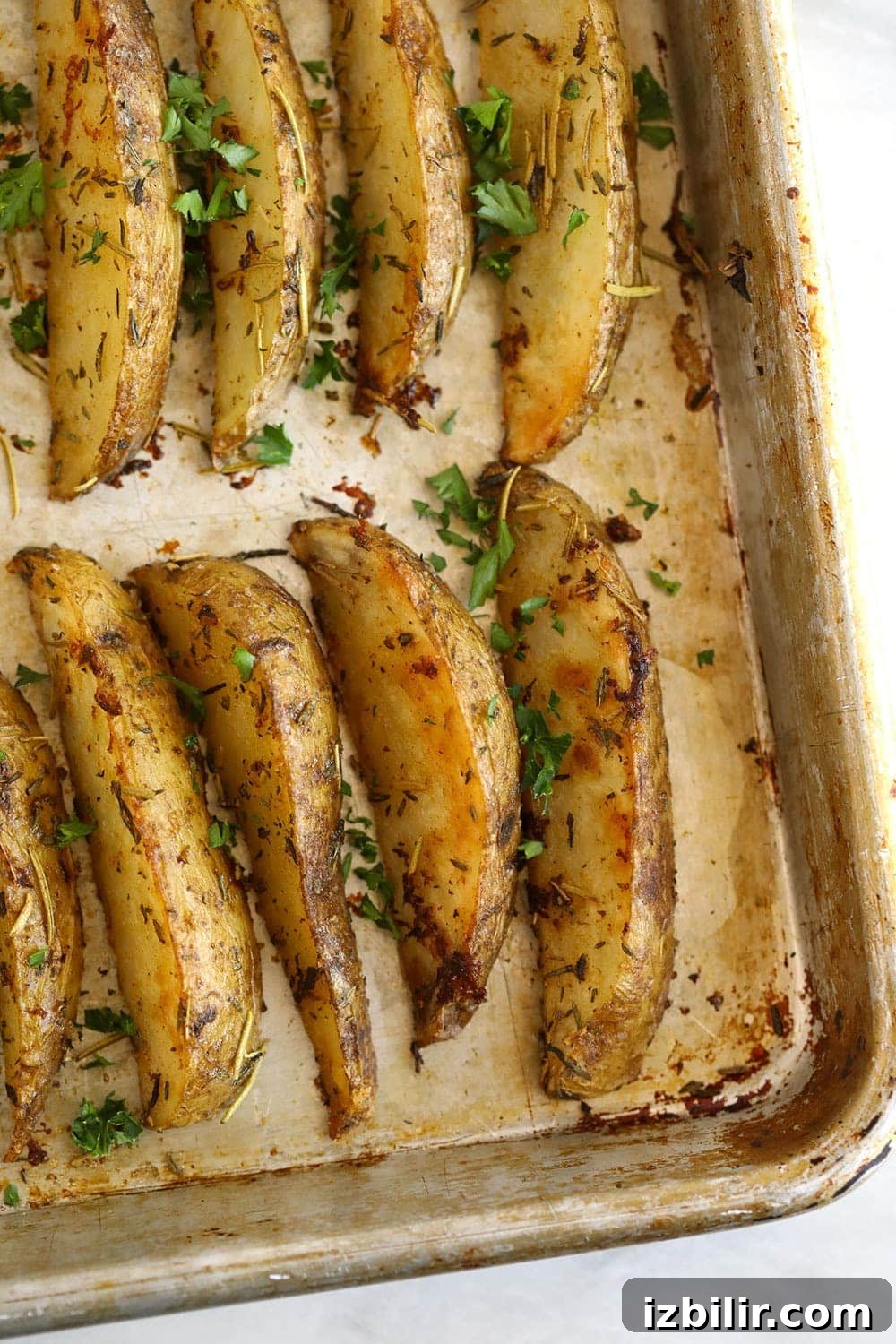 Potato wedges on a baking sheet with fresh parsley sprinkled over the potato wedges. 