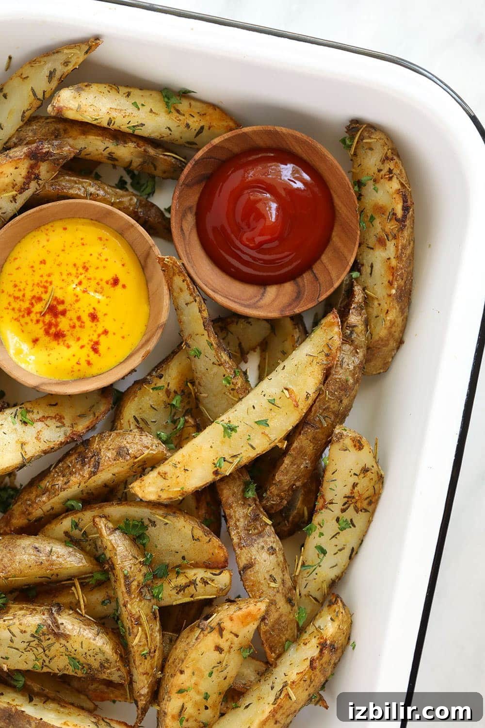 Potato wedges in a pan with ketchup and mustard. 