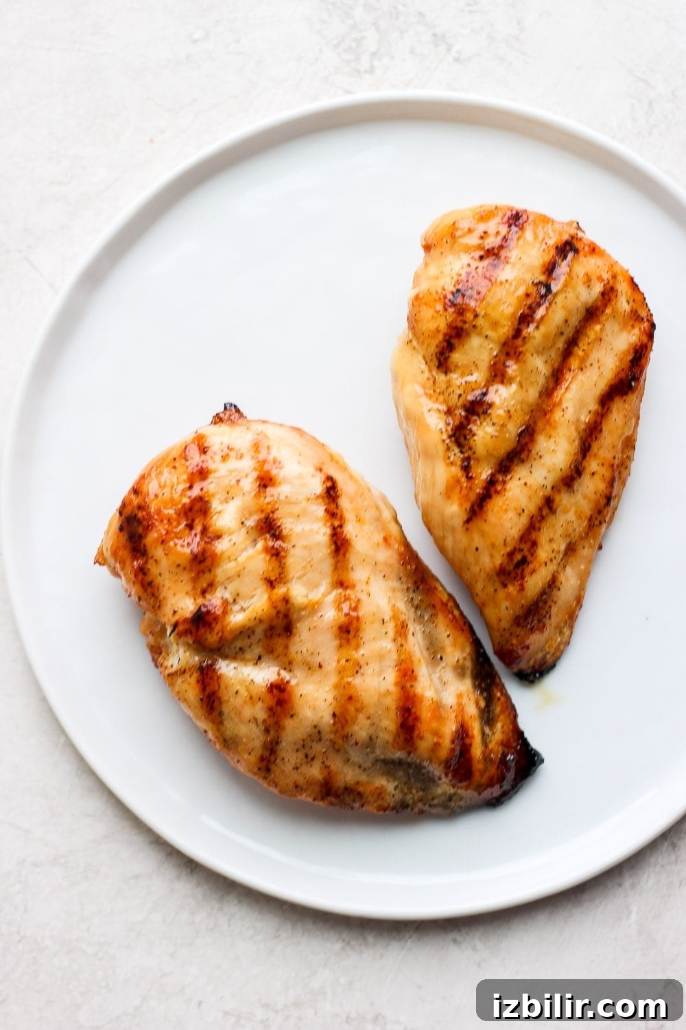 Grilled chicken breasts, ready for slicing. Two grilled chicken breasts on a plate.
