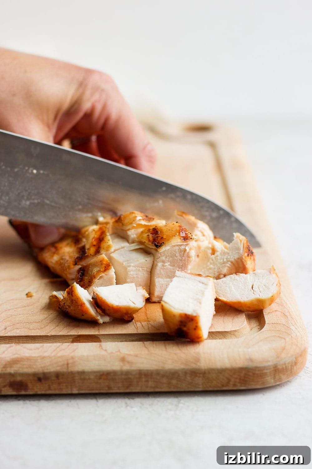 Let grilled chicken rest before slicing. Knife cutting chicken breast on a cutting board.