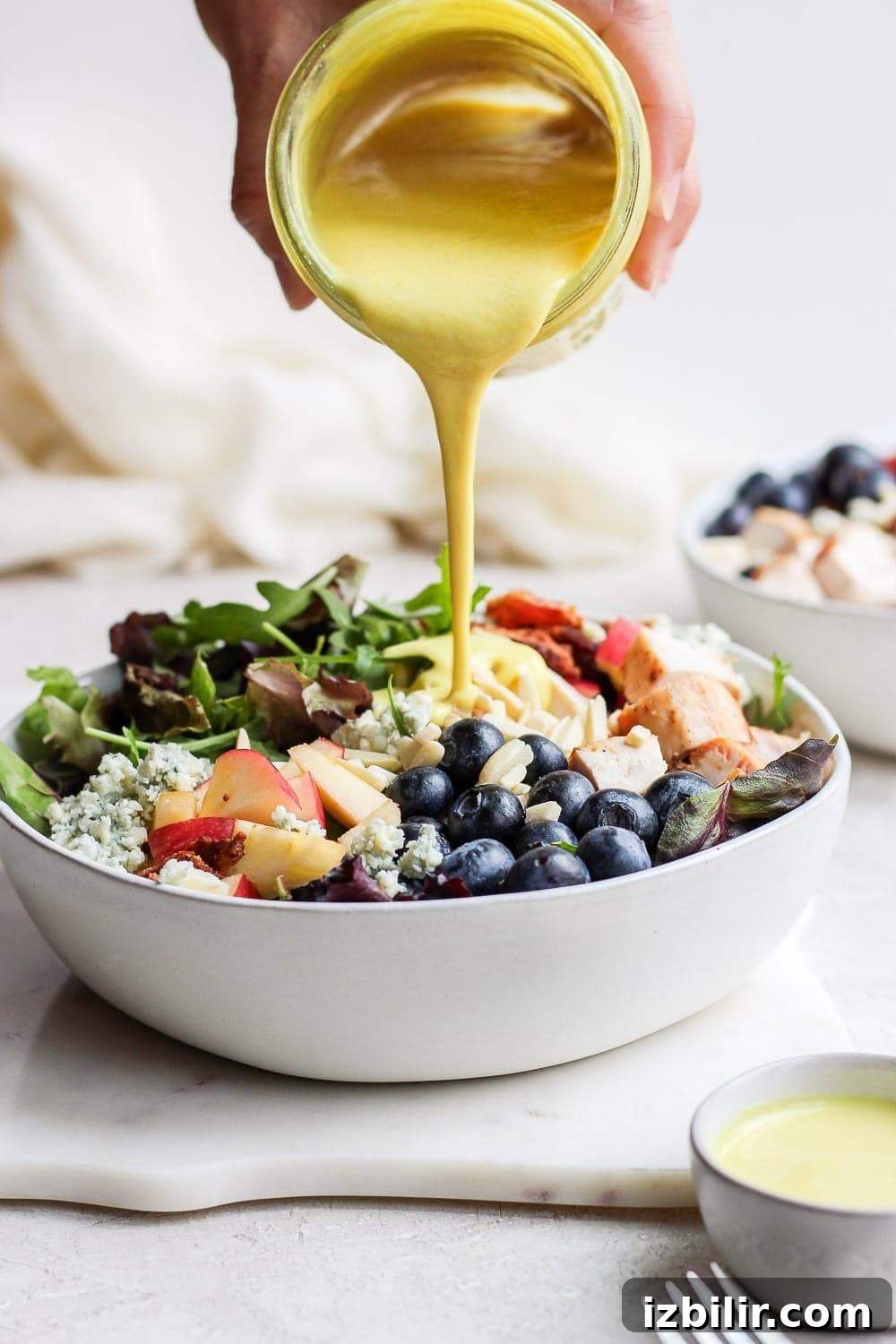 A drizzle of honey mustard completes the salad. Pouring honey mustard dressing onto chicken salad in a bowl.