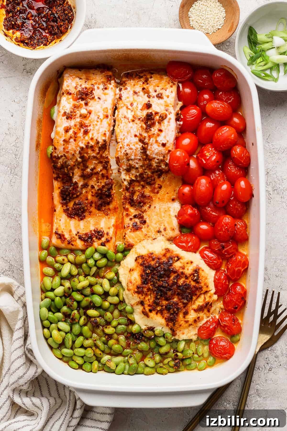 Close-up of baked chili crunch salmon with burst cherry tomatoes and edamame in a casserole dish