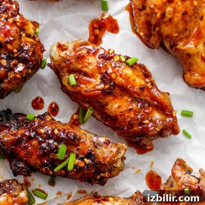 Glazed chicken wings on parchment paper garnished with sesame seeds and chopped green onions.