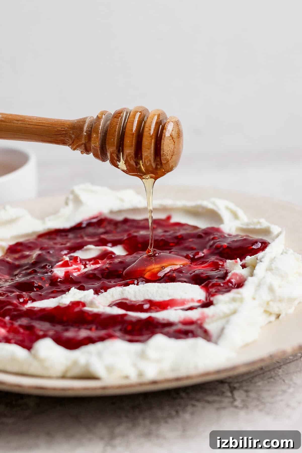 honey dipper drizzling hot honey over goat cheese dip with raspberry jam