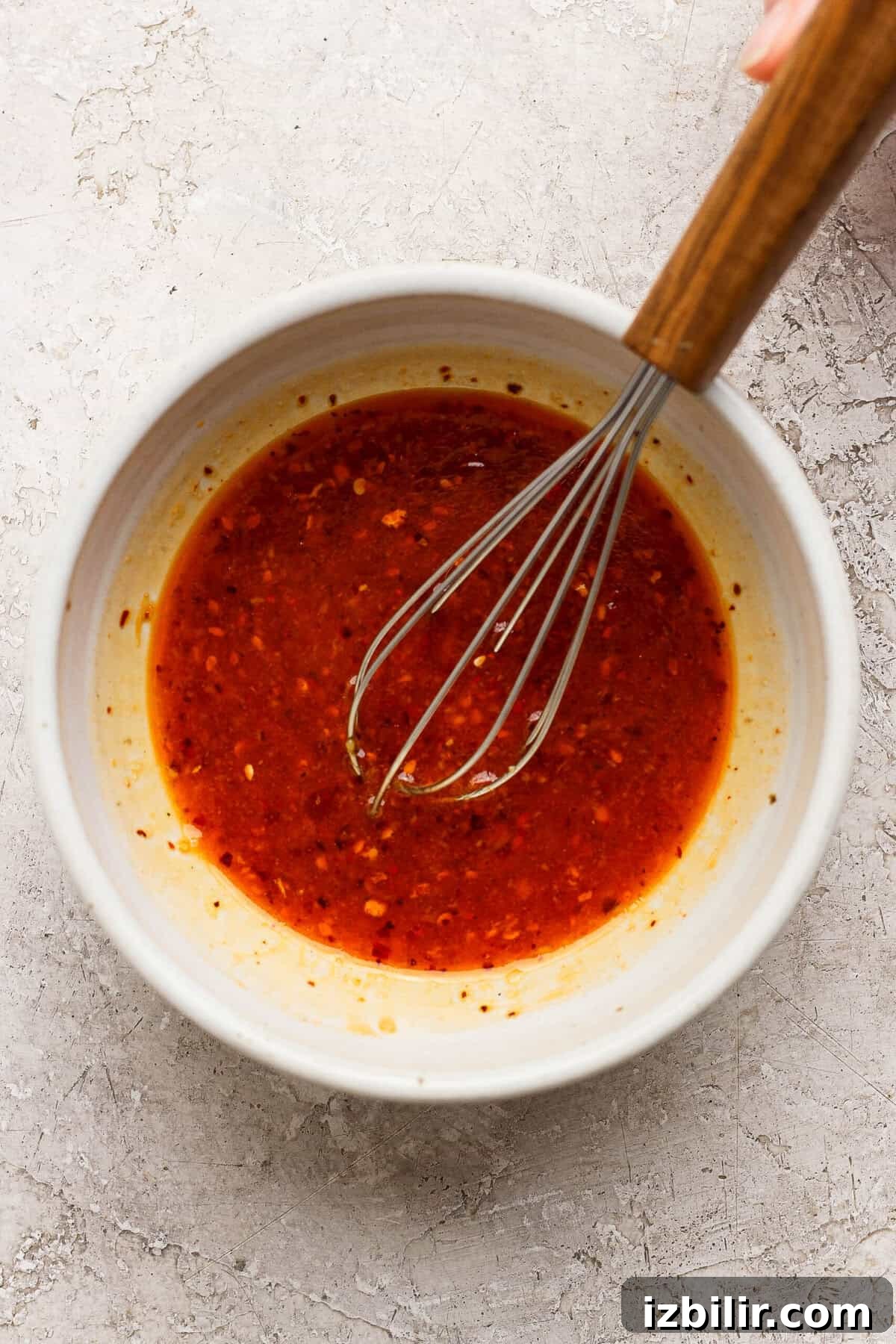 Zesty Summer Corn and Tomato Salad with Chili Crunch Dressing 3 whisking chili crunch dressing with sesame oil ginger and lime in a ceramic bowl