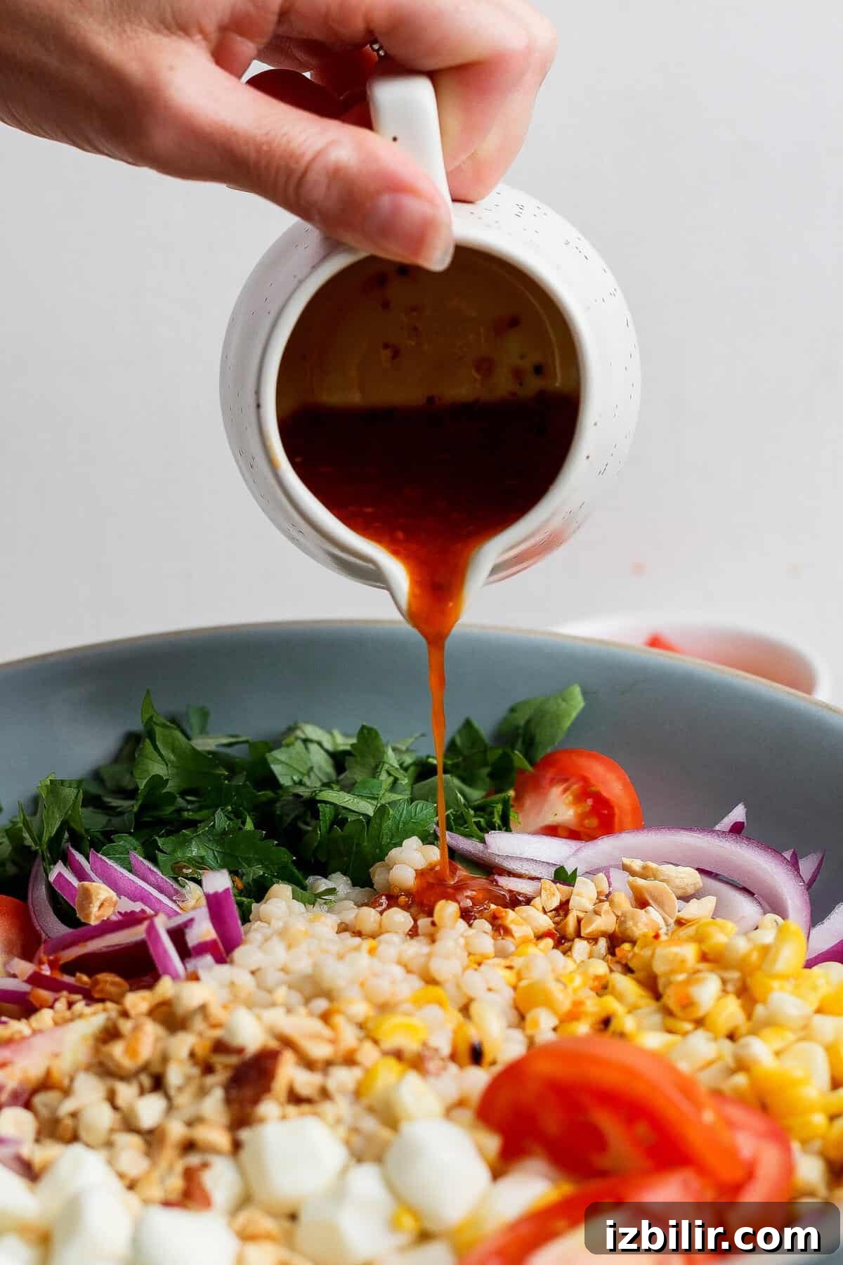 Zesty Summer Corn and Tomato Salad with Chili Crunch Dressing 4 pouring chili crunch dressing over corn tomato salad from a pitcher