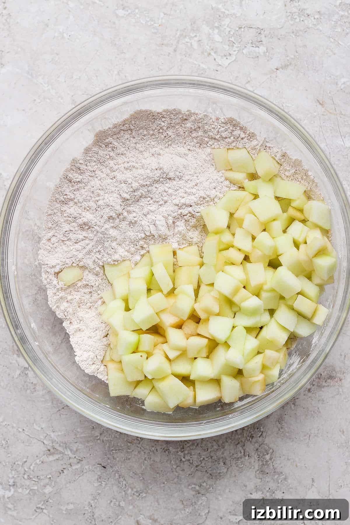 Protein-Packed Apple Muffins with Cottage Cheese 3 A glass bowl containing flour and diced green apples on a light textured surface.