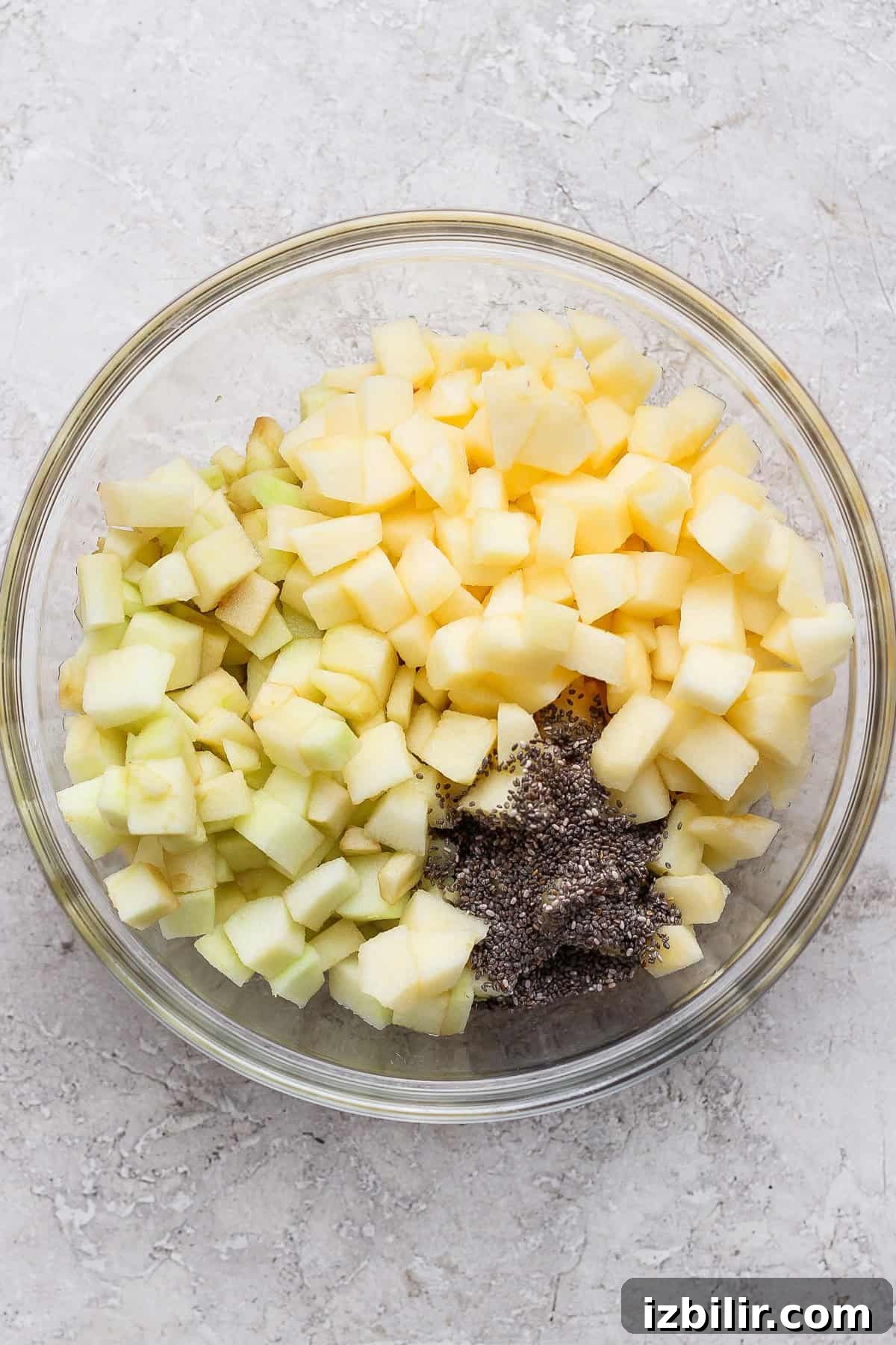 Diced apples and chia seeds in a glass mixing bowl for protein apple crisp.