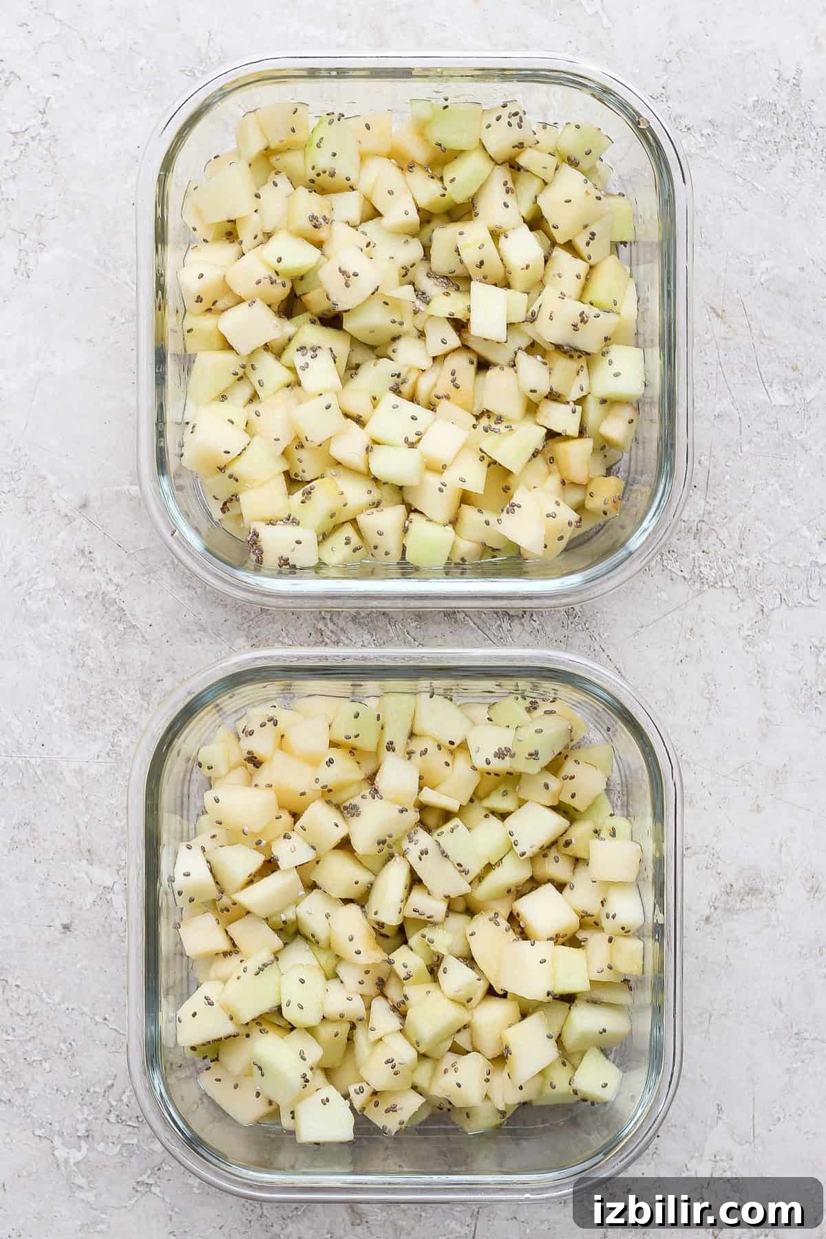 Diced apples divided between two glass meal prep containers for protein apple crisp.