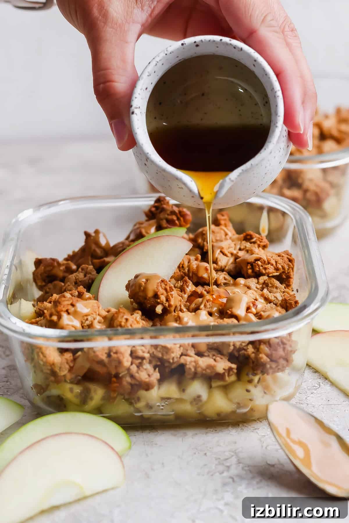 Maple syrup drizzled over an individual protein apple crisp with nut butter and apple slices.