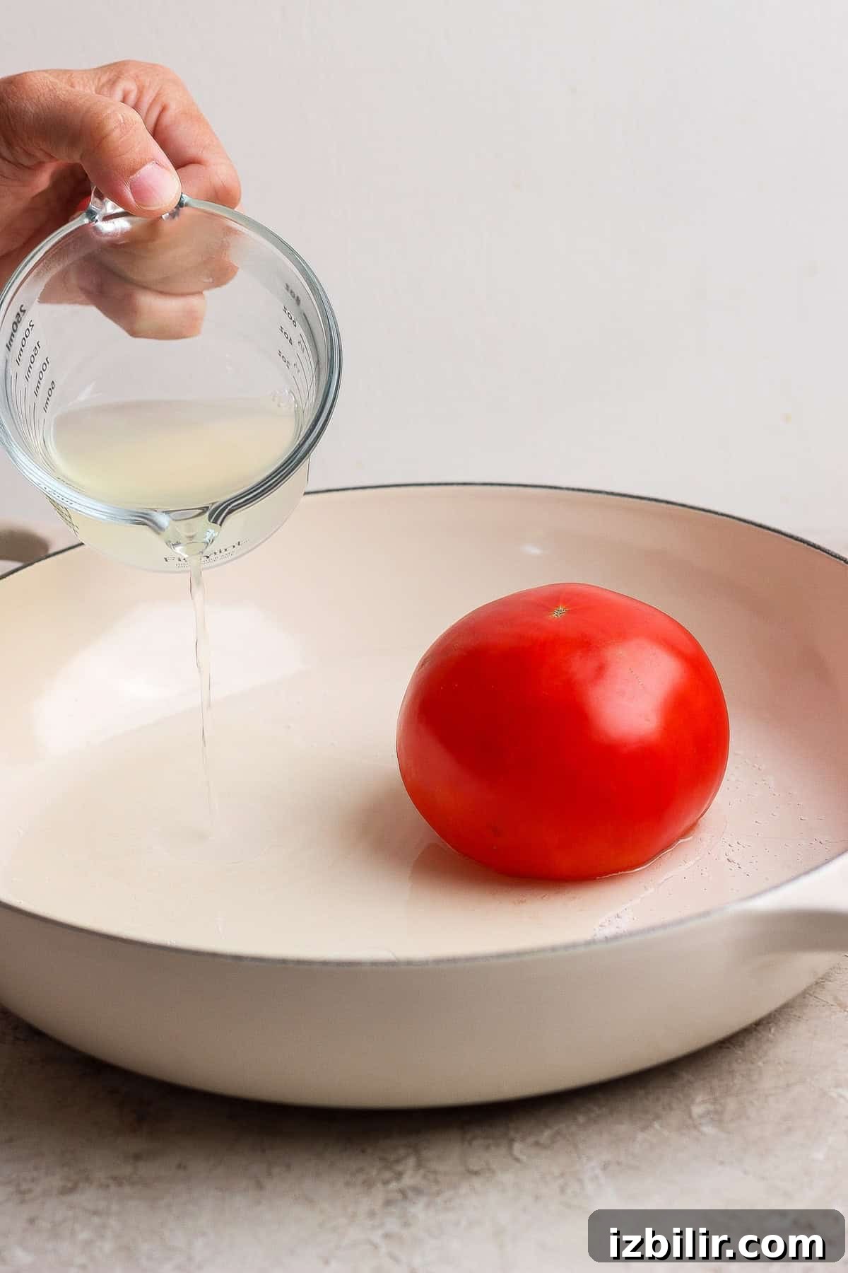 Reserved pasta water poured around a whole tomato in a skillet for steaming.