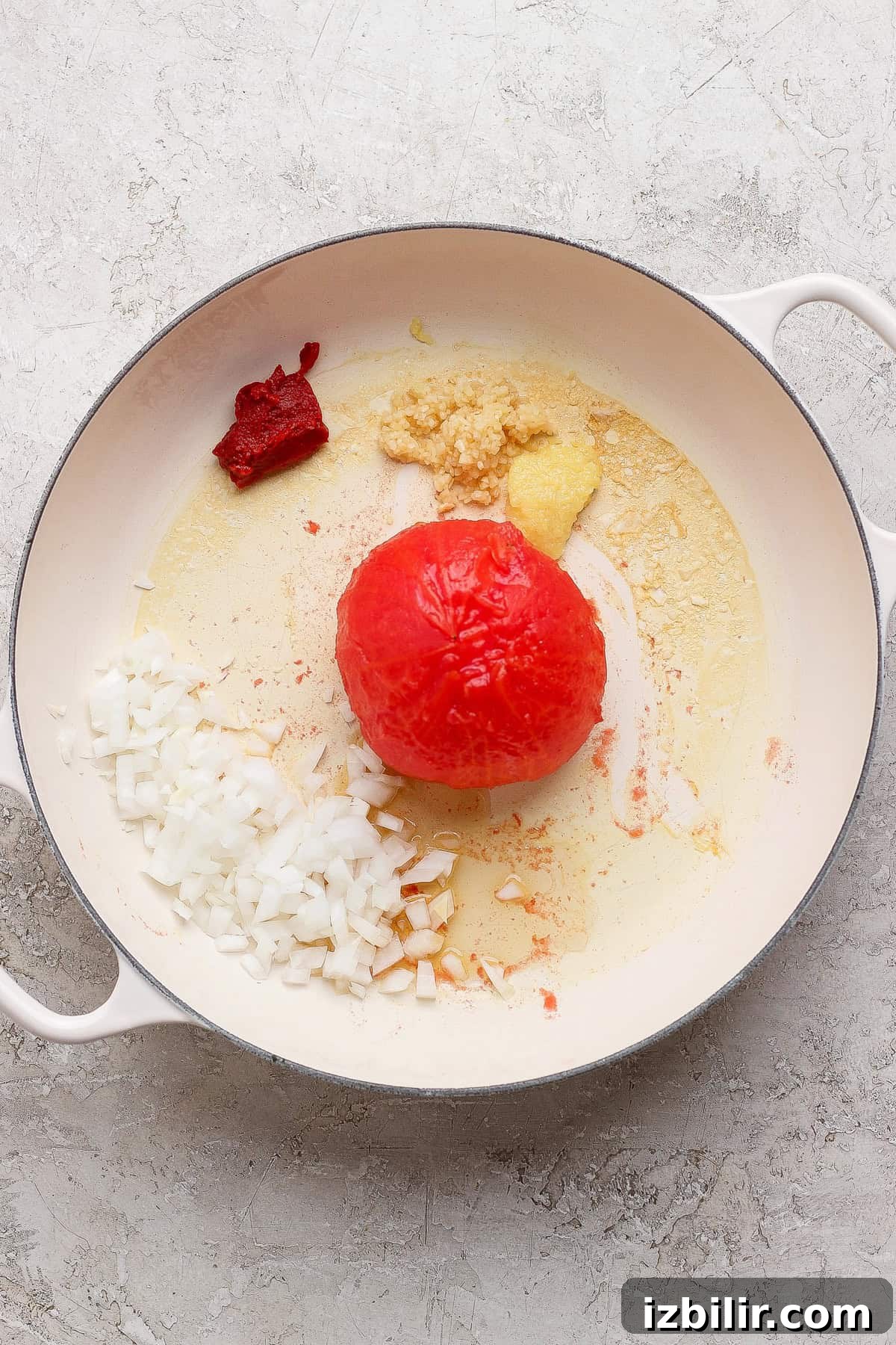 A peeled steamed tomato with diced onion, garlic, and tomato paste in a skillet.