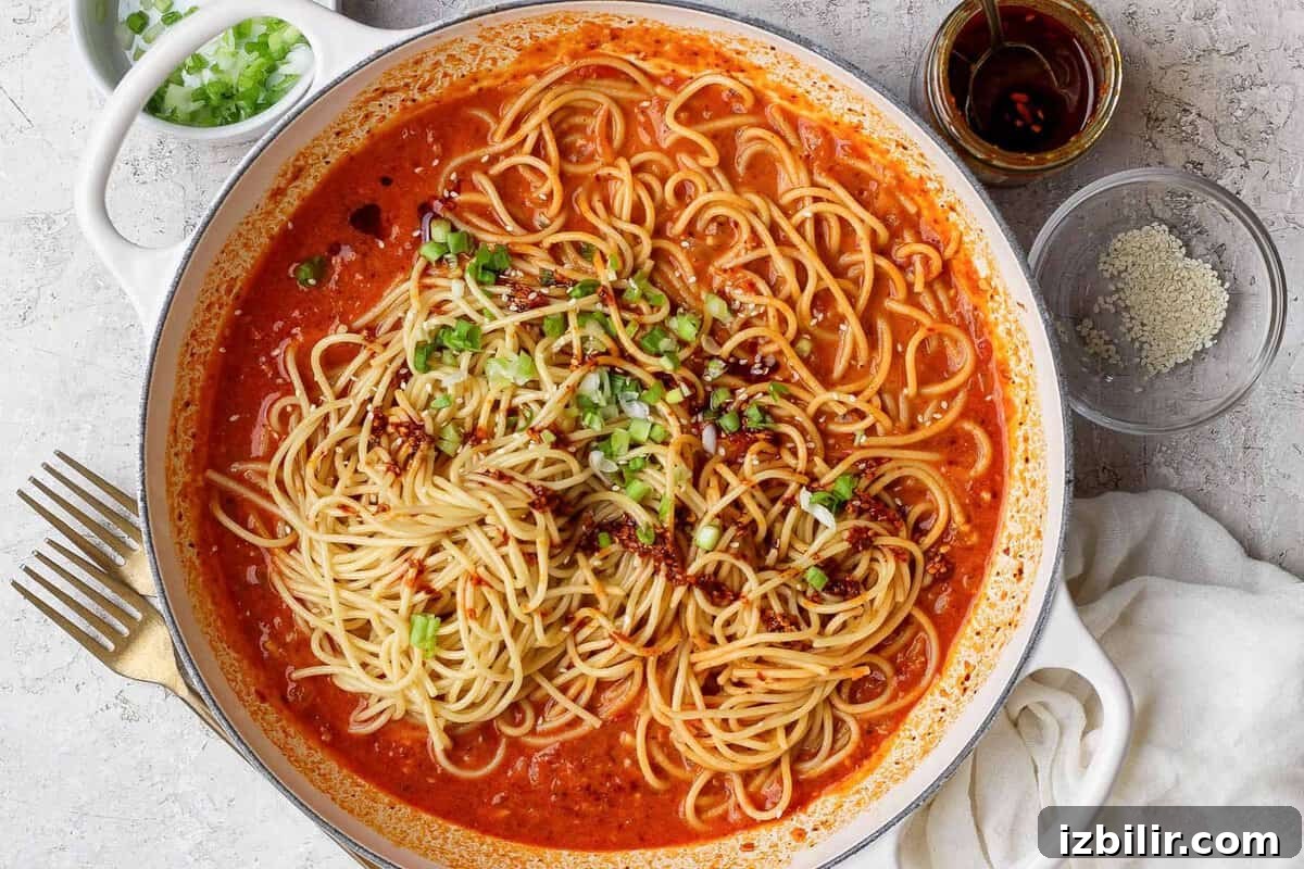 Chili crunch pasta served with green onions, sesame seeds, and extra chili crunch.