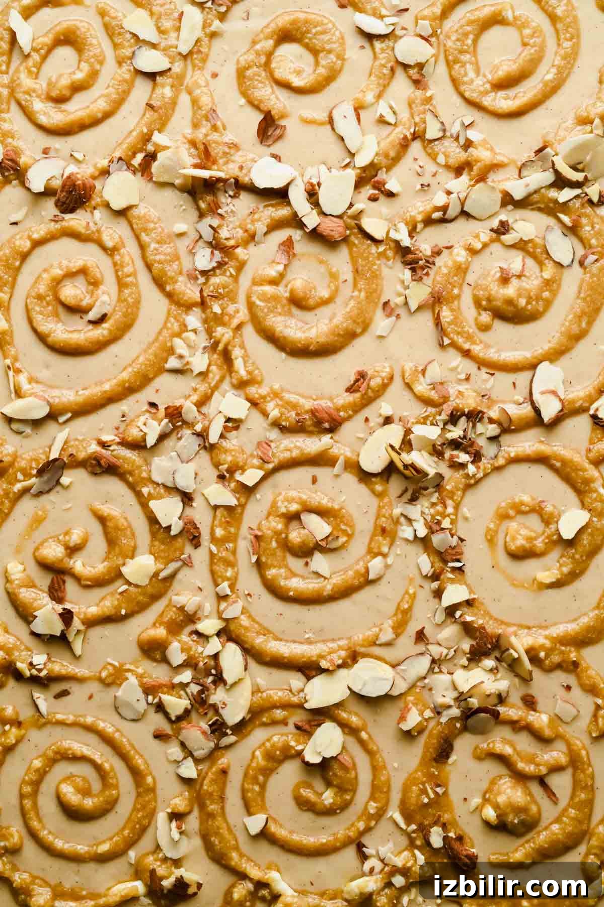 Sheet pan pancake batter topped with piped frangipane swirls and sliced almonds before baking.