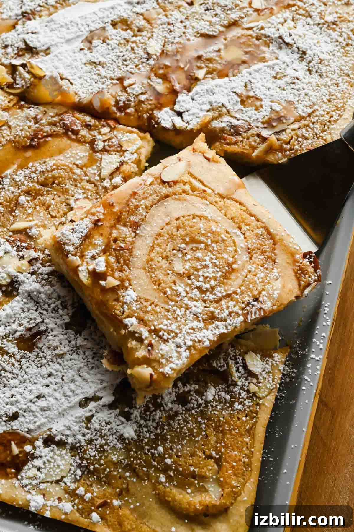 Golden square of sheet pan almond croissant pancake with a frangipane swirl, sliced almonds, and powdered sugar.