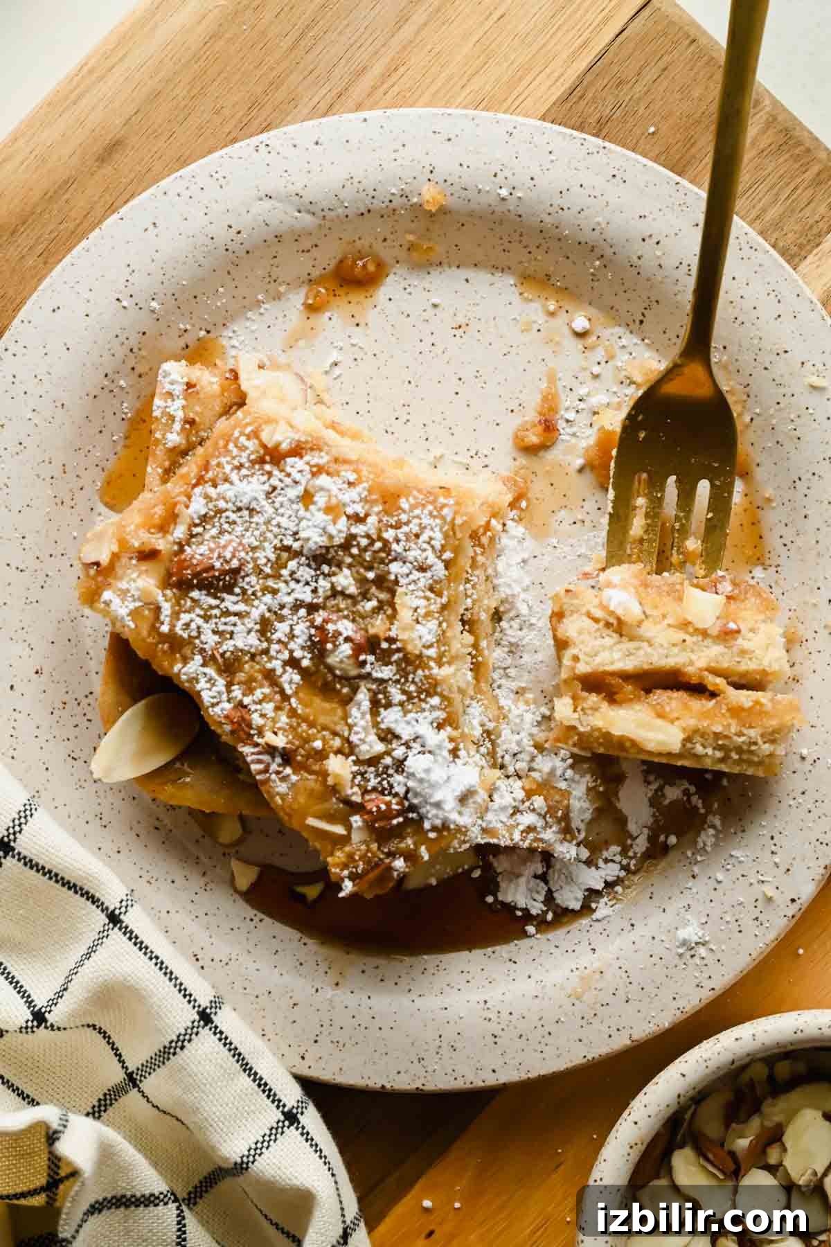 Almond croissant sheet pan pancake squares served with maple syrup and powdered sugar.
