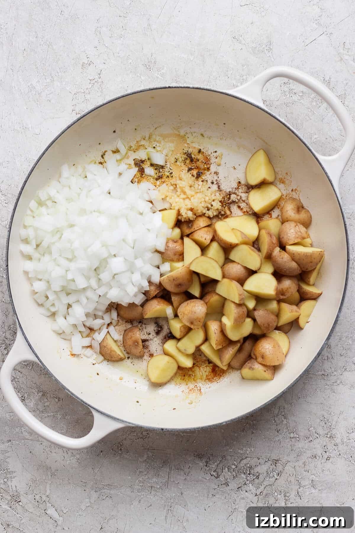 Apple Cider-Glazed Chicken Thighs Recipe 4 Diced white onion, minced garlic, and quartered baby potatoes in a white skillet.