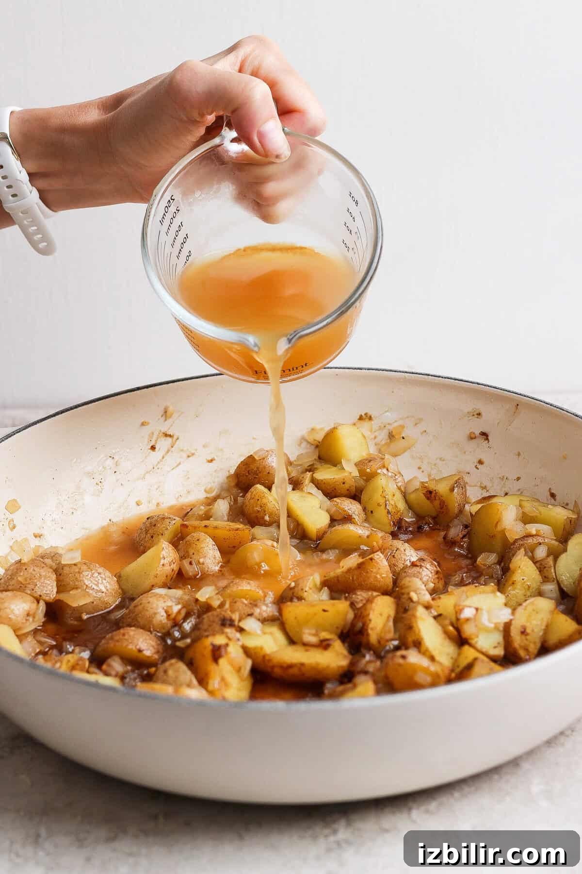 Apple Cider-Glazed Chicken Thighs Recipe 5 Apple cider being poured into a skillet of browned baby potatoes, onion, and garlic.