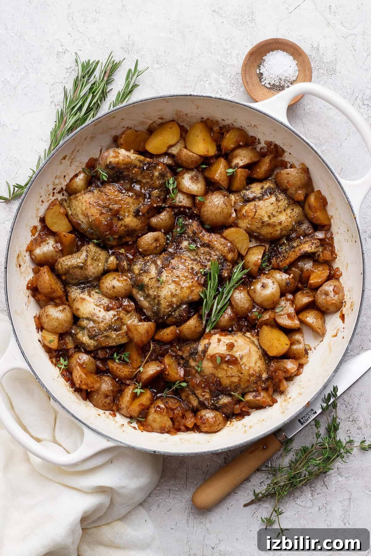 Apple Cider-Glazed Chicken Thighs Recipe 7 Overhead view of apple cider chicken thighs and baby potatoes in a white skillet with rosemary and thyme.
