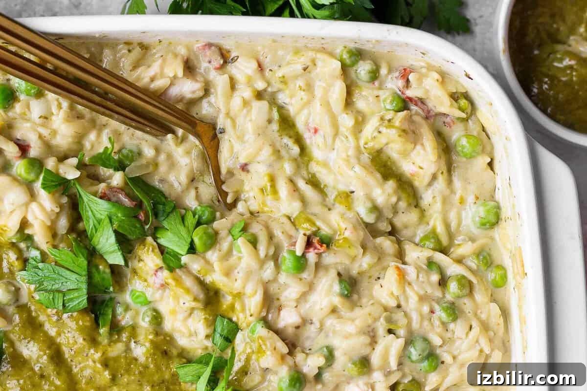 Dump-and-Bake Pesto Chicken Orzo 8 Close-up of creamy chicken pesto orzo with peas, sun-dried tomatoes, pesto, and fresh parsley.
