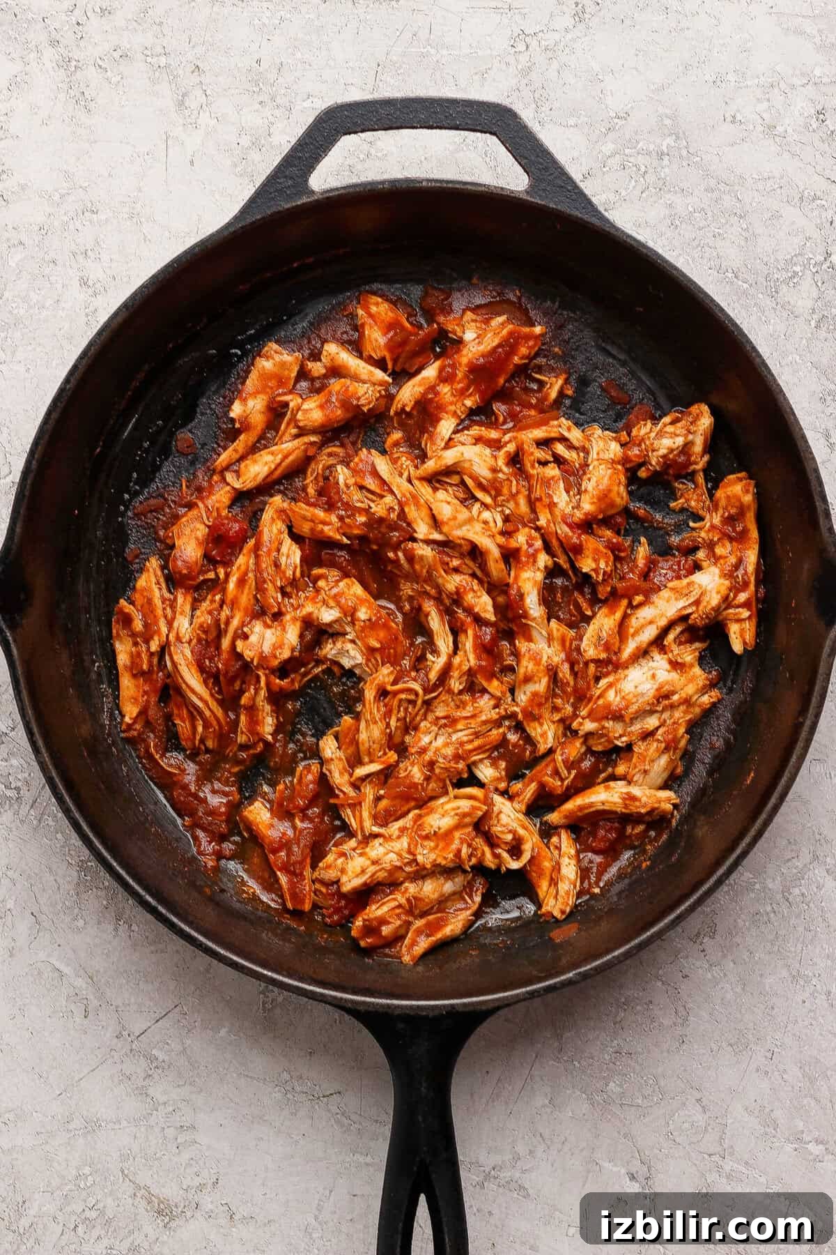Oven-Baked Street Corn Chicken Tacos 4 Shredded cooked chicken coated in red taco cooking sauce in a cast-iron skillet.