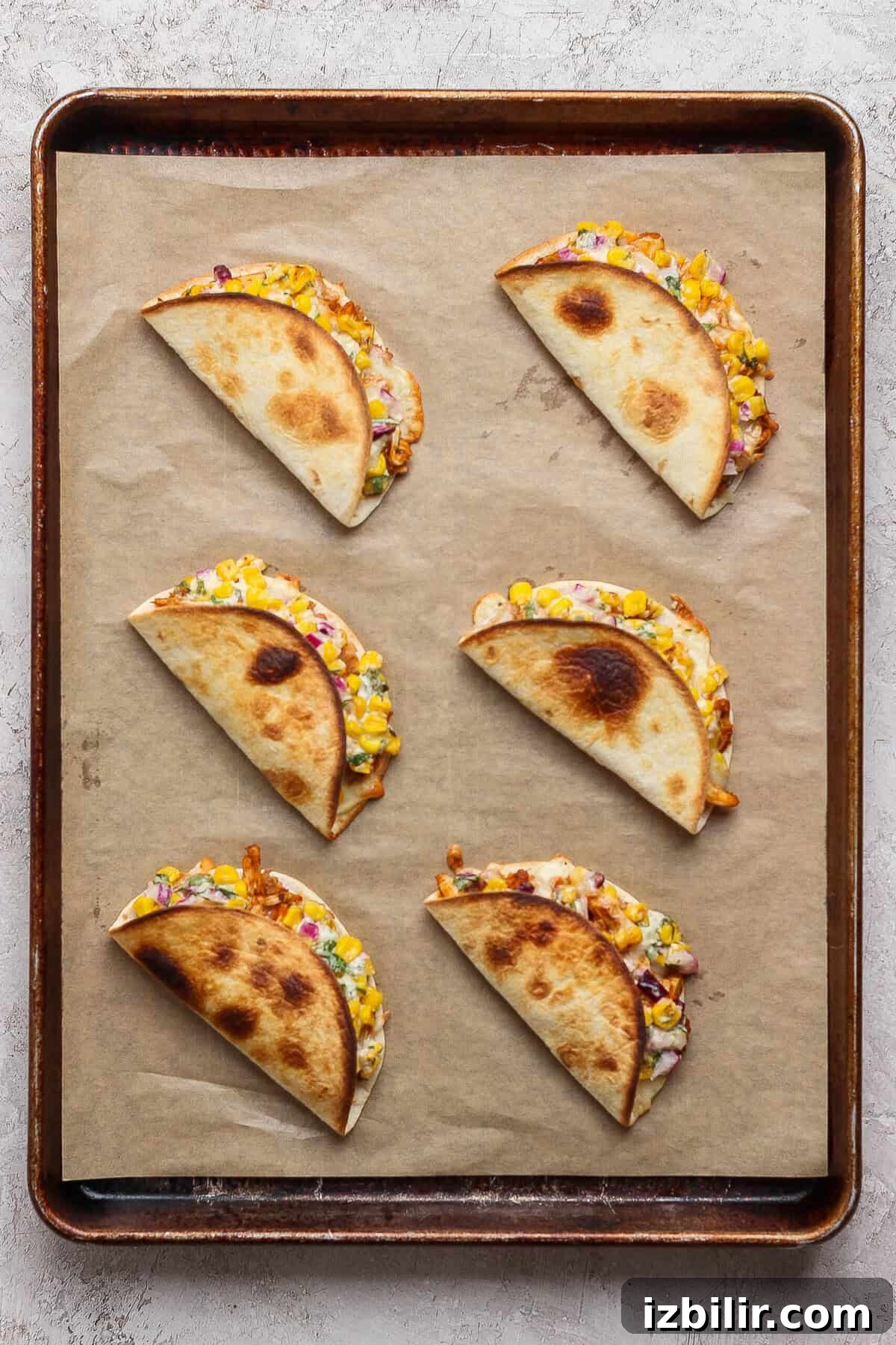 Oven-Baked Street Corn Chicken Tacos 6 Six folded street corn chicken tacos baked until golden on a parchment-lined metal sheet pan.