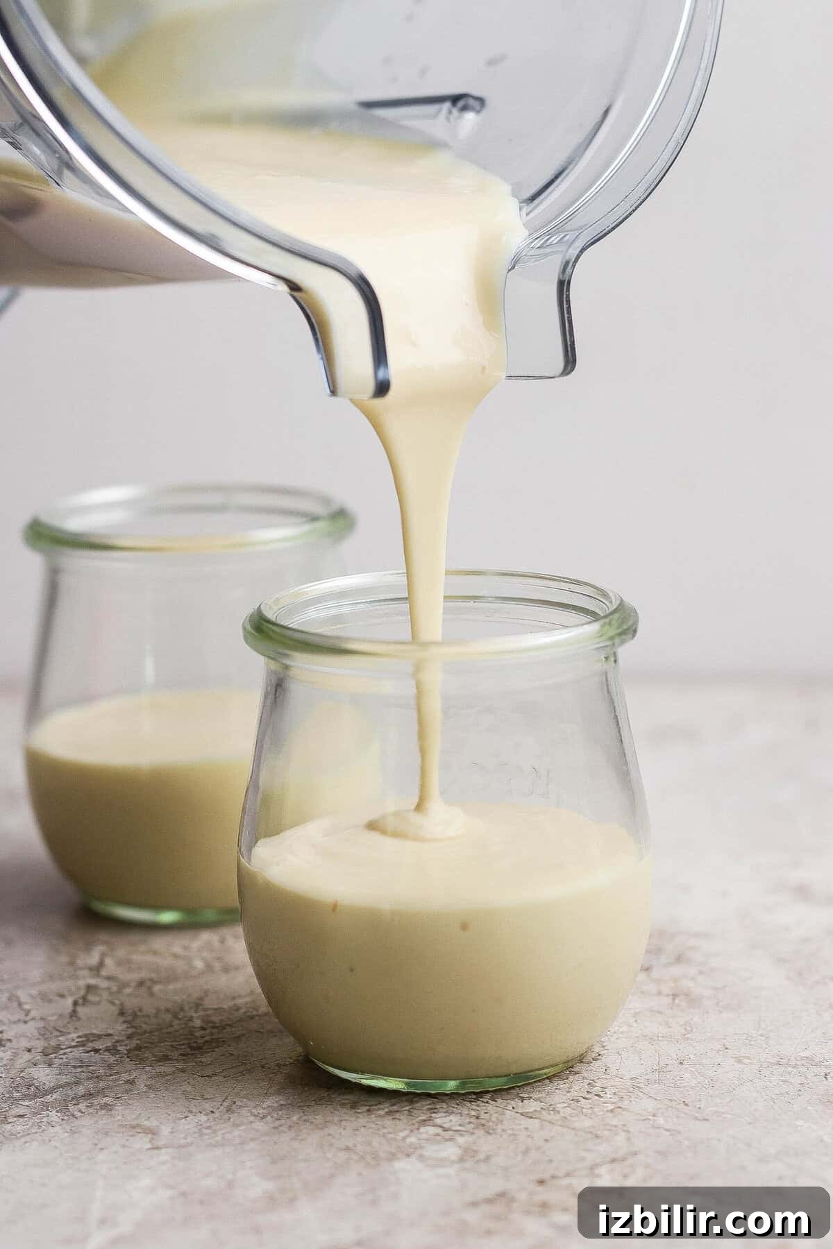 High-Protein Snickers Cheesecake Cups Recipe 4 Blended cottage cheese cheesecake mixture being poured into individual clear dessert jars.