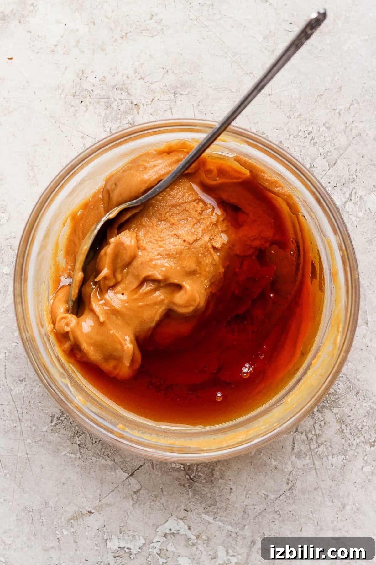 High-Protein Snickers Cheesecake Cups Recipe 5 Creamy peanut butter and maple syrup being stirred together in a small glass bowl.