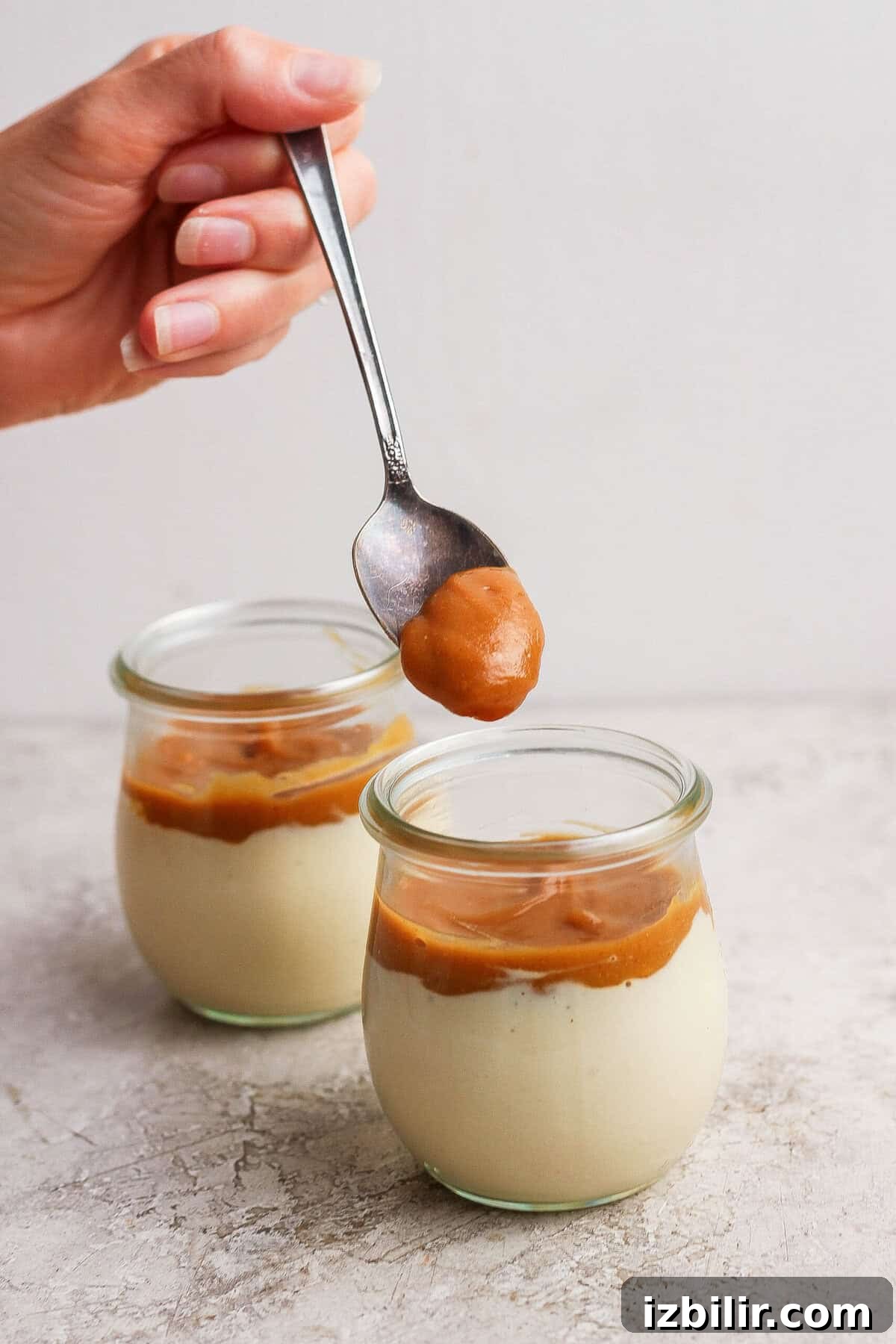 High-Protein Snickers Cheesecake Cups Recipe 6 Maple peanut butter being spooned over the cottage cheese layer in individual dessert jars.