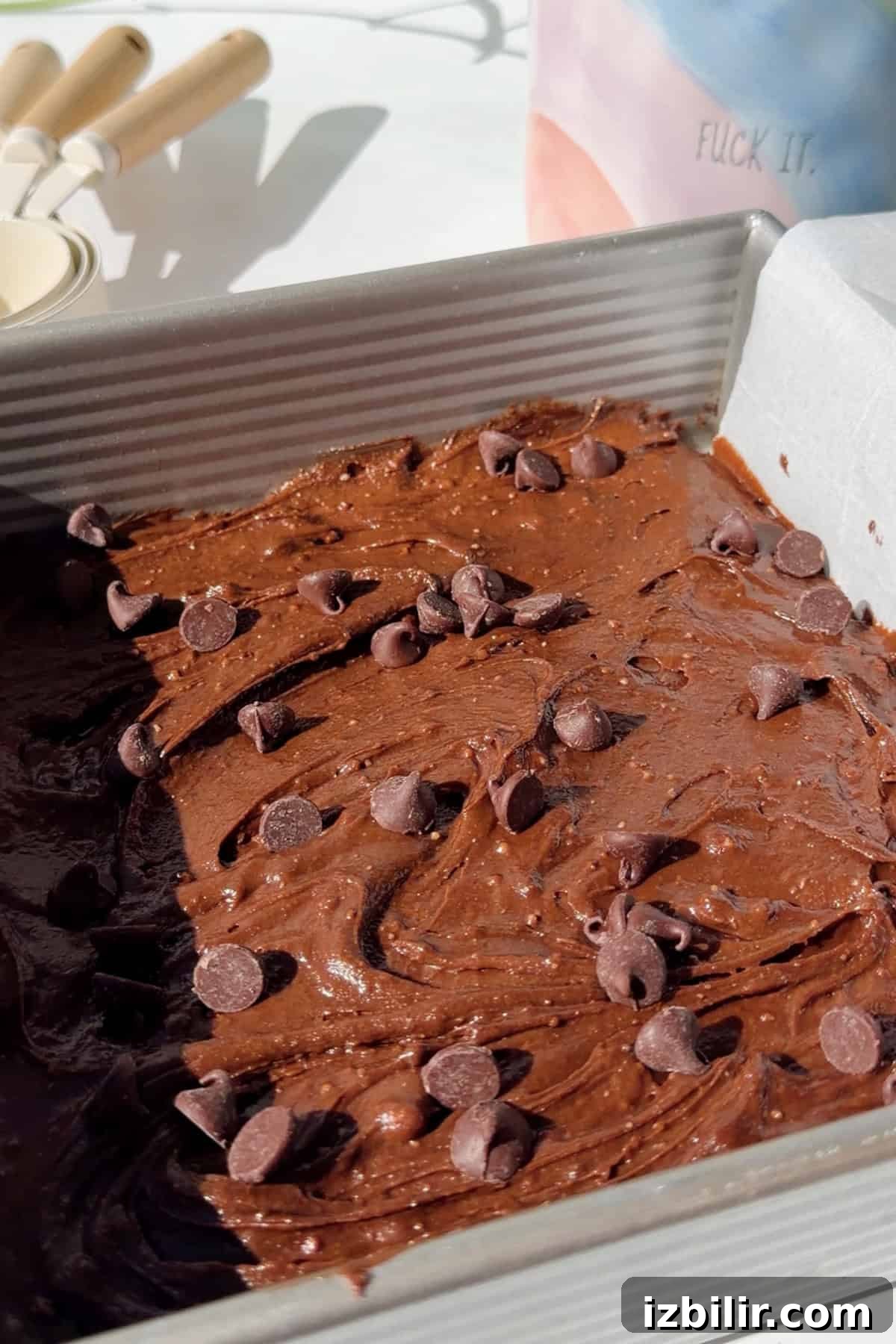Fudgy 2-Ingredient Cottage Cheese Brownies 4 Thick cottage cheese brownie batter spread in a square metal baking pan and topped with chocolate chips before baking.