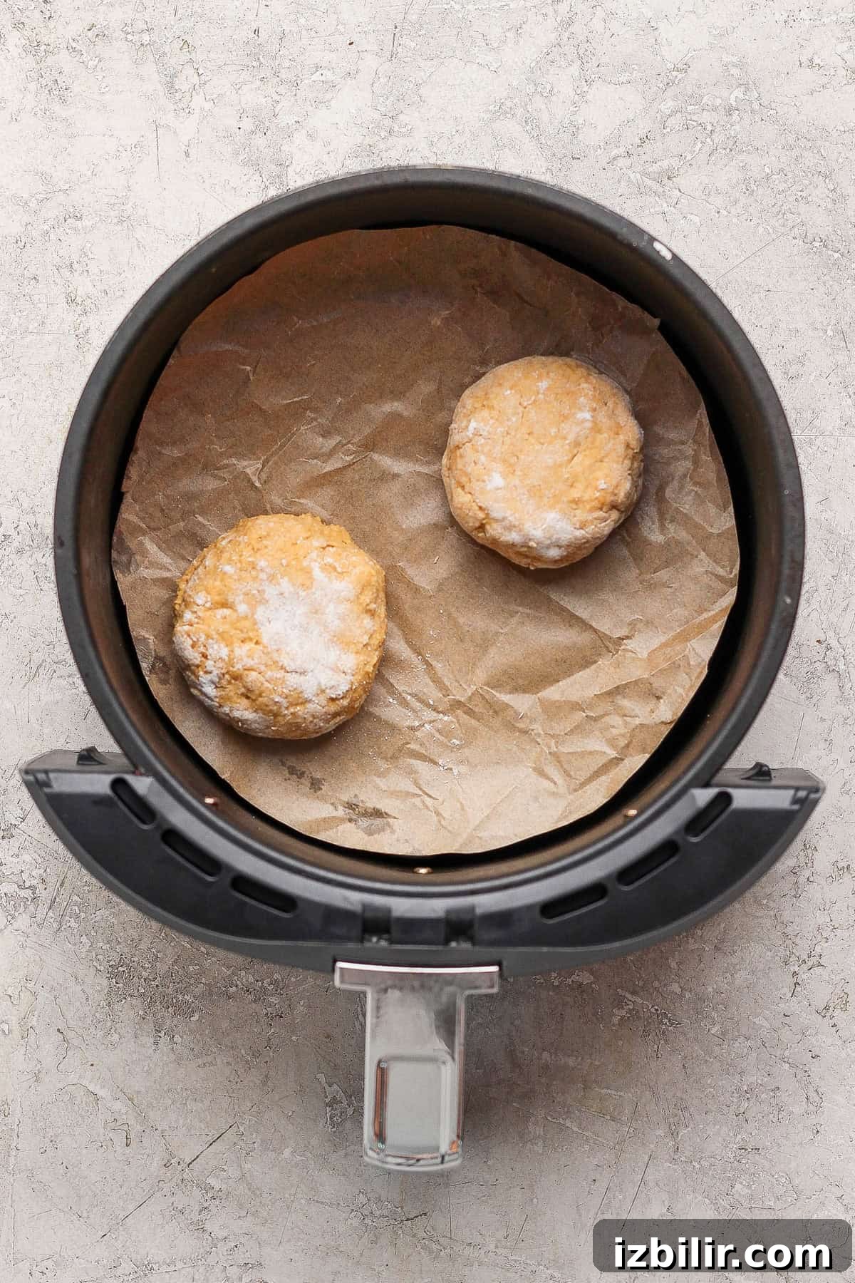 Crispy Cottage Cheese Pumpkin Fritters Recipe 7 Two shaped uncooked pumpkin fritters on parchment paper inside an air fryer basket.