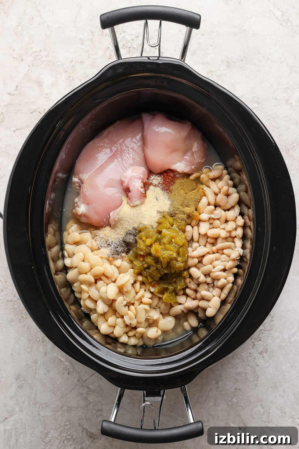 Raw chicken, white beans, green chiles, vinegar, and spices loaded into a slow cooker.