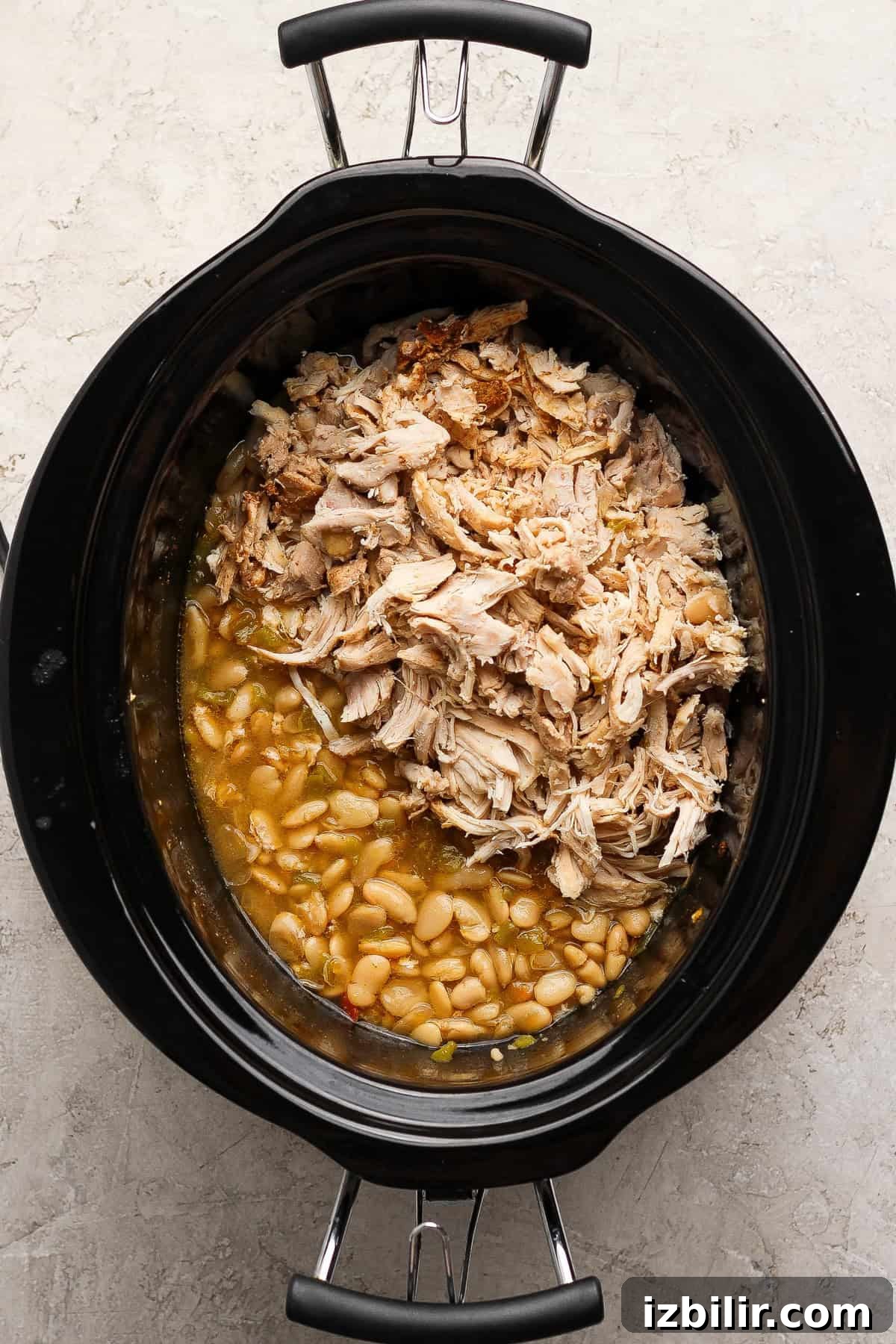 Shredded chicken returned to a slow cooker with butter beans and cannellini beans.