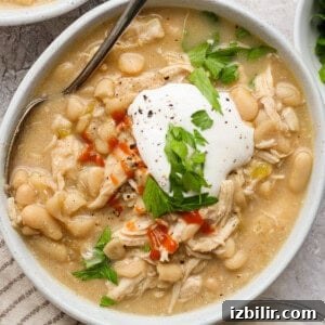 Bowl of crockpot white chicken chili with chicken, butter beans, cottage cheese, hot sauce, and fresh herbs.